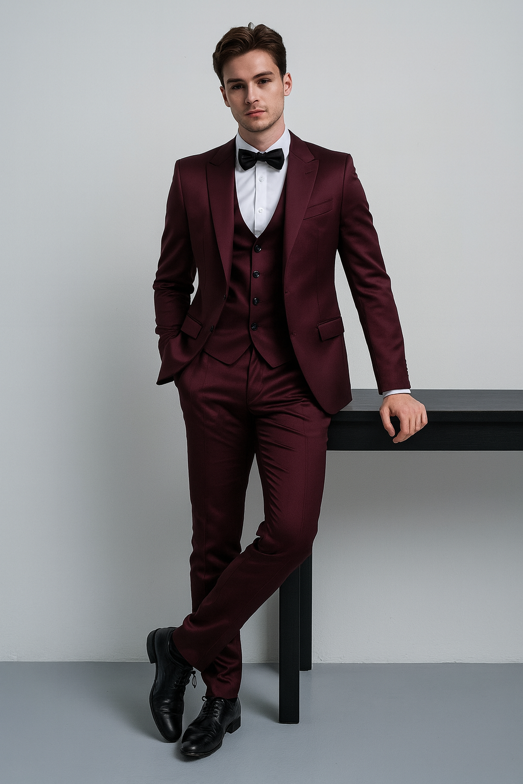 A dark-haired man stands dressed in an elegant dark red designer suit and a black bow tie.